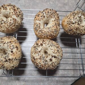 Five everything sourdough bagels cooling on a wire rack with sesame seeds poppy seeds garlic and onion topping
