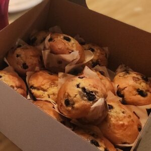 Two bakery boxes filled with fresh jumbo blueberry muffins in parchment liners on a wooden table.