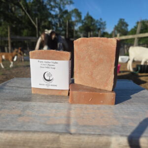Warm Amber Nights goat milk soap bars displayed outdoors at Moon Tree Farm with goats in the background