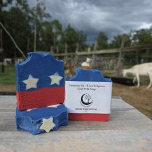 American Pie goat milk soap bars in red, white, and blue with goats in the background at Moon Tree Farm.
